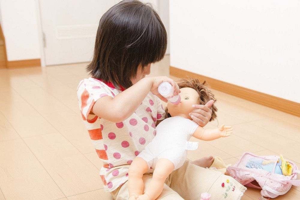 ままごとで赤ちゃんの人形にミルクをあげている女の子
