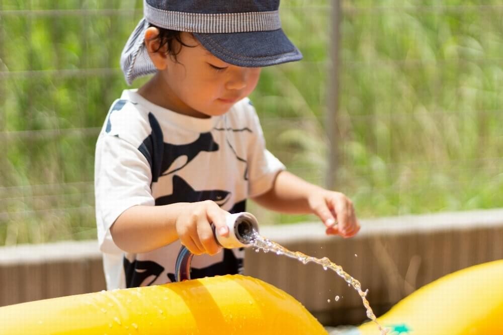 プールにホースで水を入れる男の子